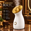 A white and gold steam care device sits on a polished marble countertop in a luxurious bathroom setting, with steam rising from its opening. The background features warm, golden-toned mirrors and vanity lighting, and the left side includes promotional text and skincare props.